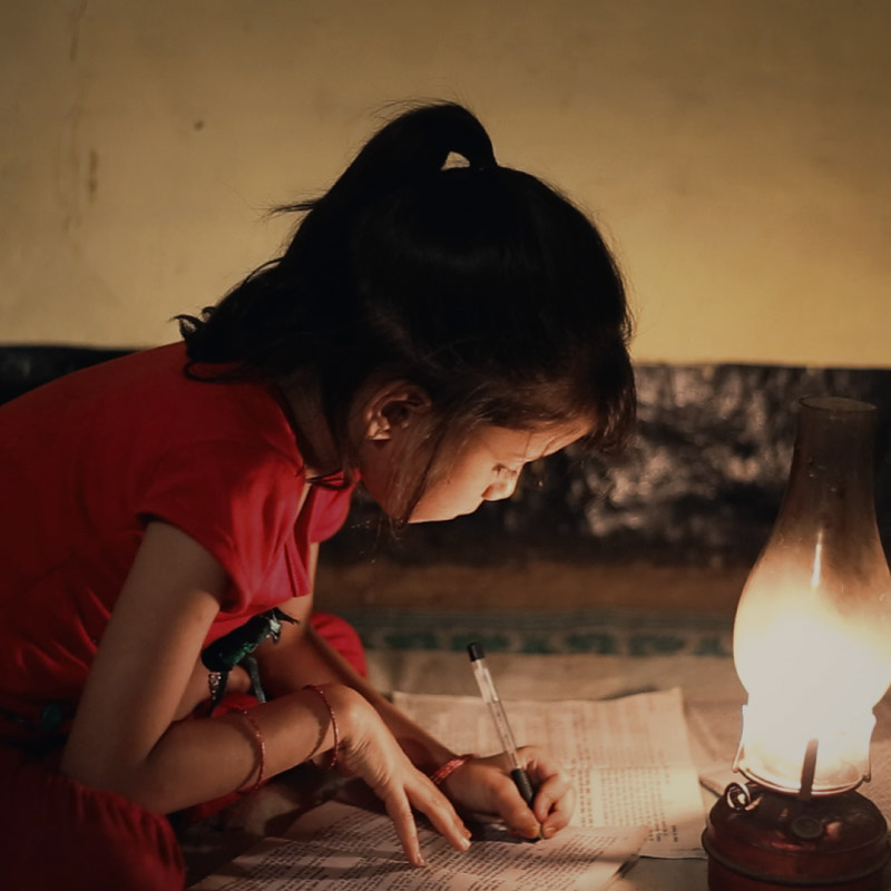 girl doing homework using the light of a lantern