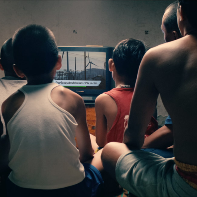 young boys huddled around a television on the floor watching news about renewable energy